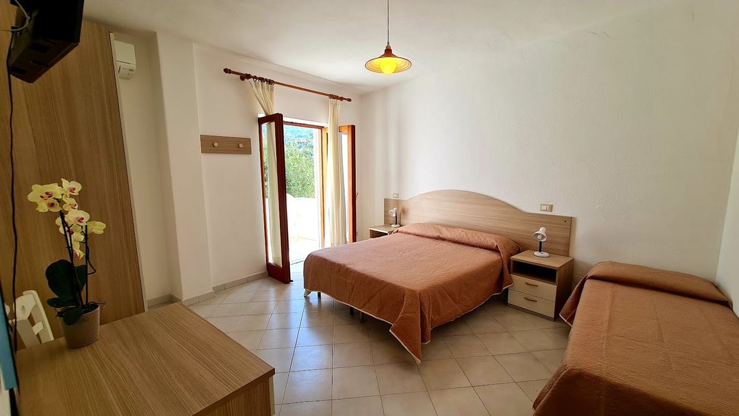 A spacious hotel bedroom with wooden furnishings, terracotta bedding, and access to an outdoor terrace.