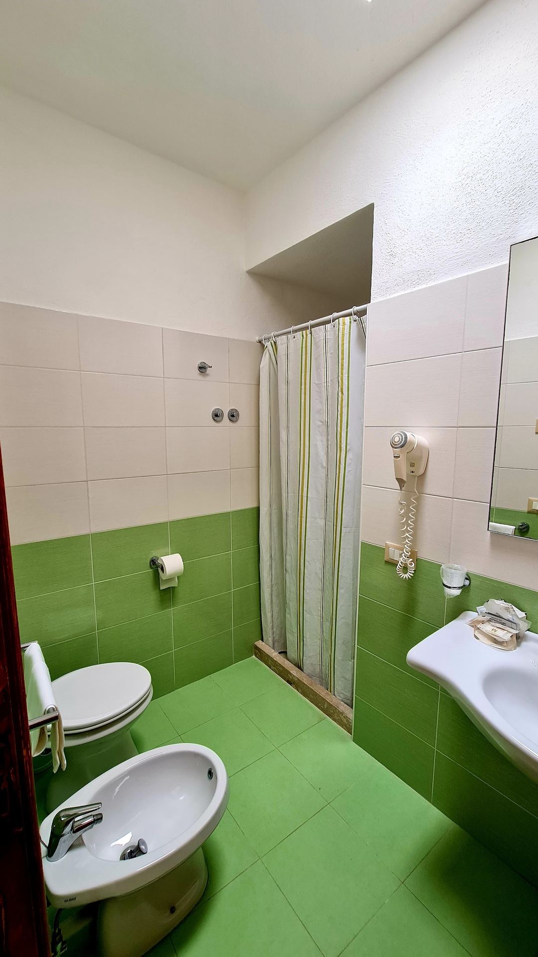 A bathroom with bright green tile flooring, white upper walls, and modern fixtures including a shower with curtain, toilet, bidet, and sink.